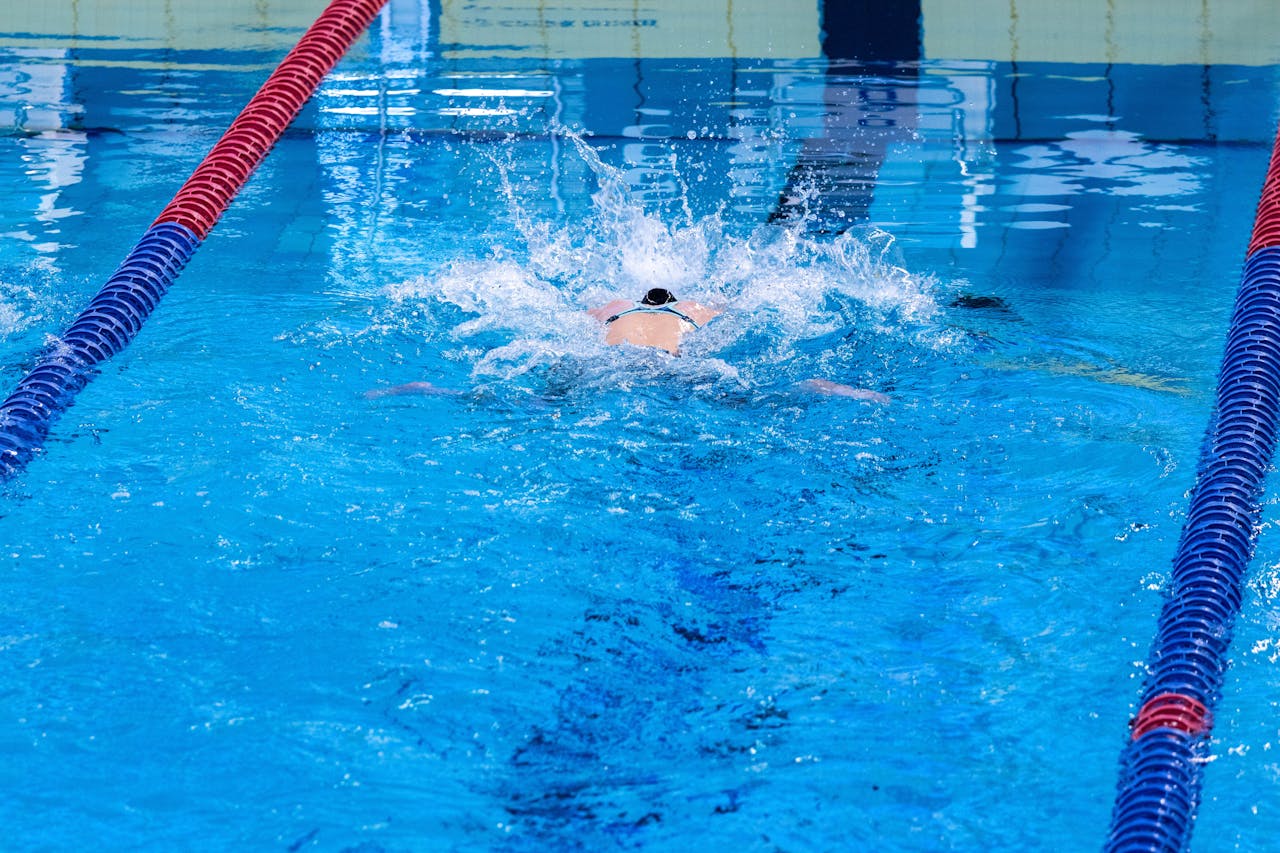 Swimmer doing backstroke in an indoor pool, showcasing competitive swimming technique.